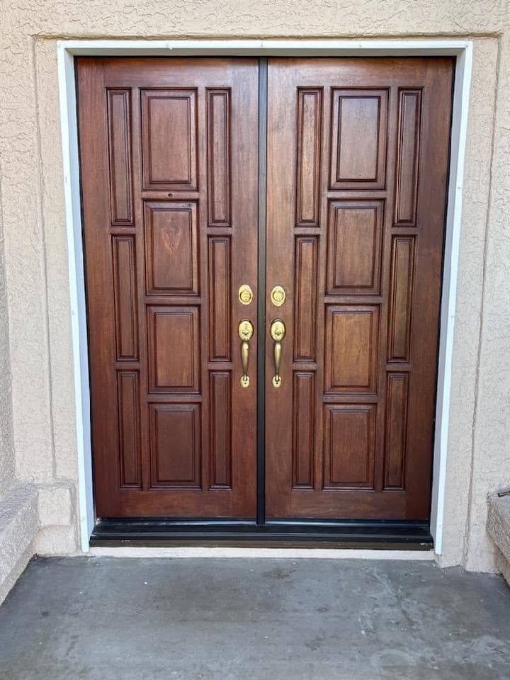 Brown wooden double doors with brass handles, set in a tan frame, on a concrete surface.