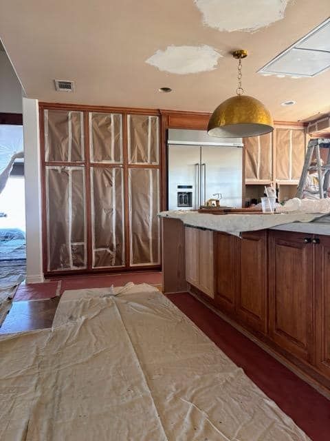 Kitchen under renovation; brown cabinets covered with plastic, gold pendant light, and protective floor coverings.