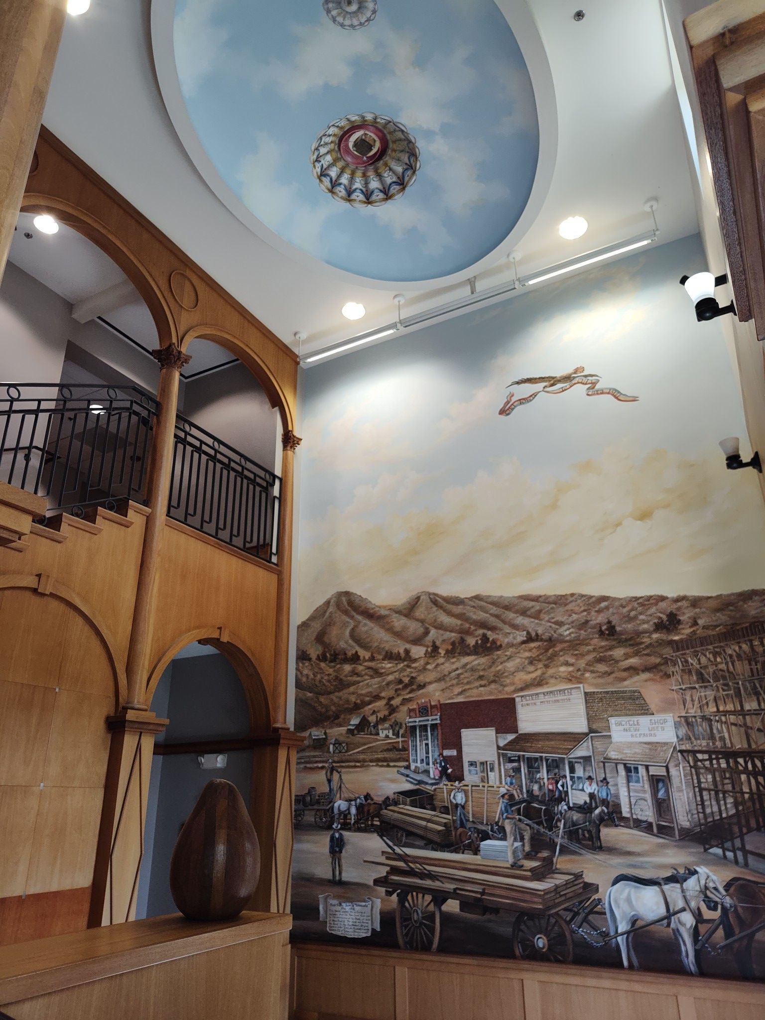Interior with a mural of a town, arches, and a painted sky on the ceiling.