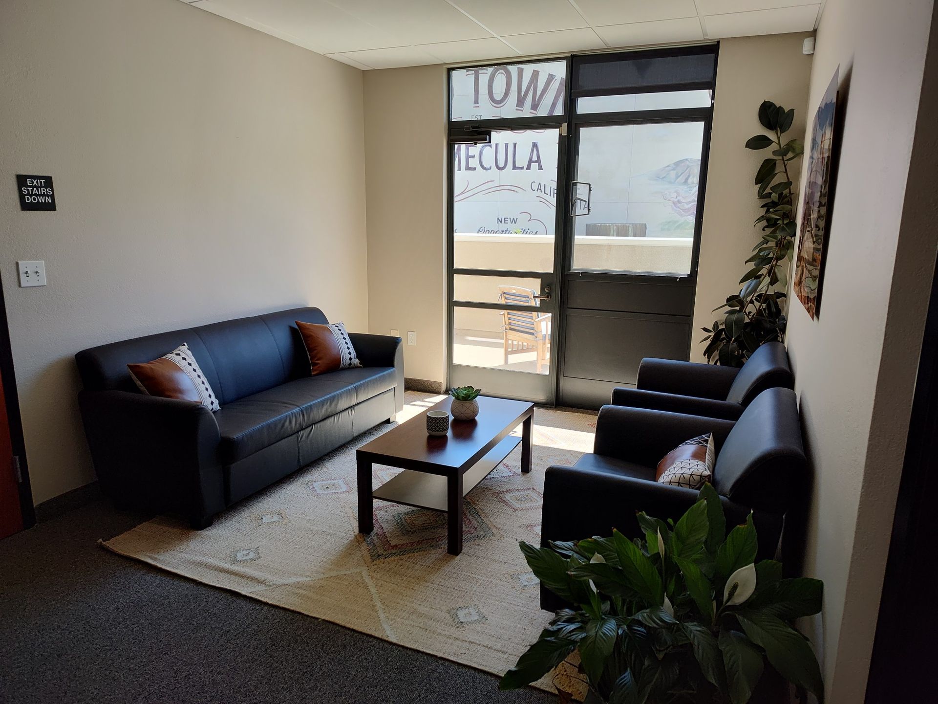 Waiting area with a black sofa, two chairs, a coffee table, and a door to the outside.