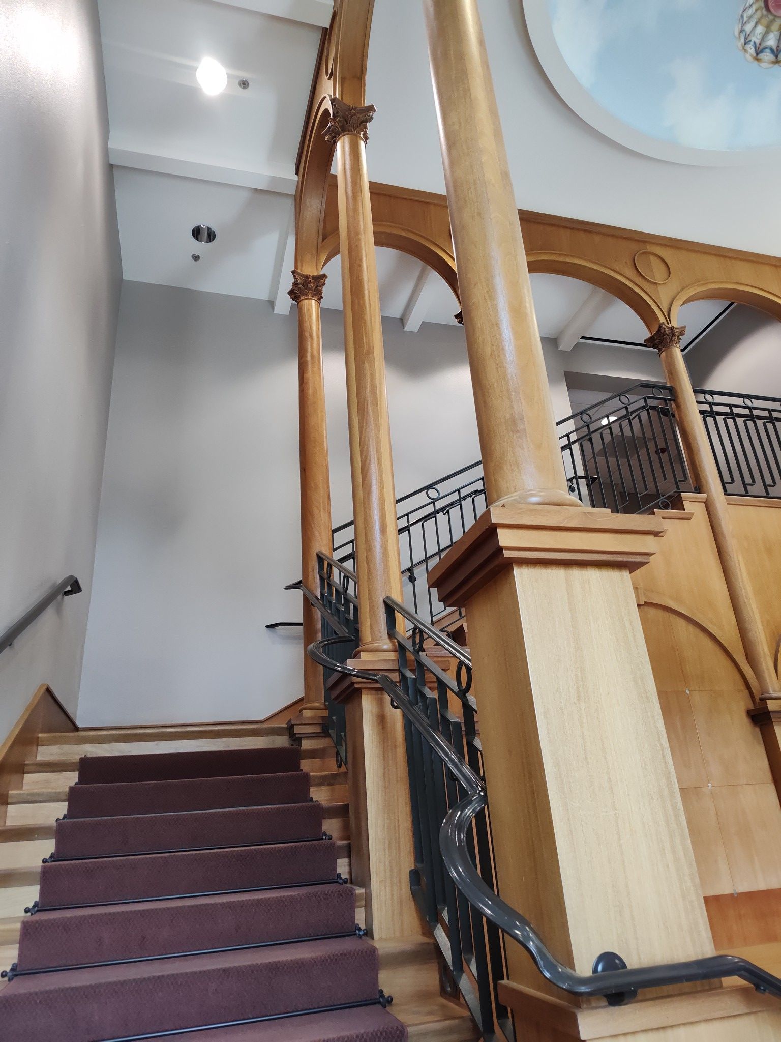 Staircase with brown carpet and wooden columns, leading up to a dome ceiling.
