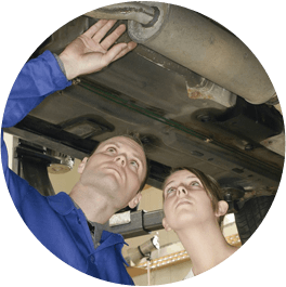 Two mechanics inspecting a vehicle’s underside on a lift, one pointing while both look upward