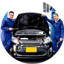 Two mechanics in blue coveralls stand beside a black car with its hood open in a service bay