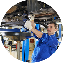 Mechanic in blue coveralls working under a raised car in an auto repair shop