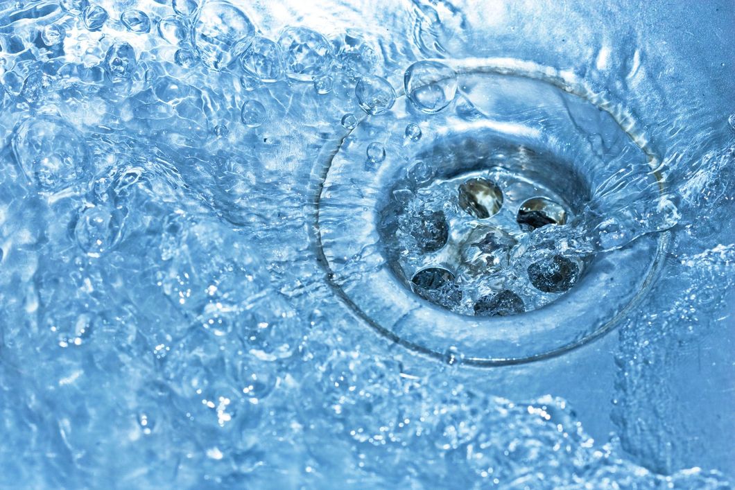 Close-up of a chrome drain with swirling blue water and ice crystals