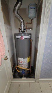 Gas water heater with vent pipe and expansion tank in a narrow closet.