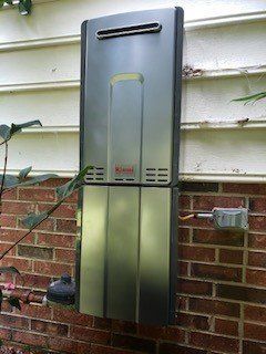Wall-mounted metallic outdoor heater with a vent, installed on a brick house exterior.