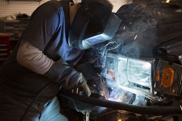 Mechanic welding a car headlight at night, bright sparks lighting the front bumper