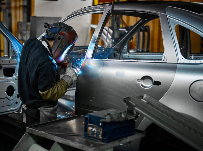 Worker welding the side of a silver car body in an auto manufacturing workshop