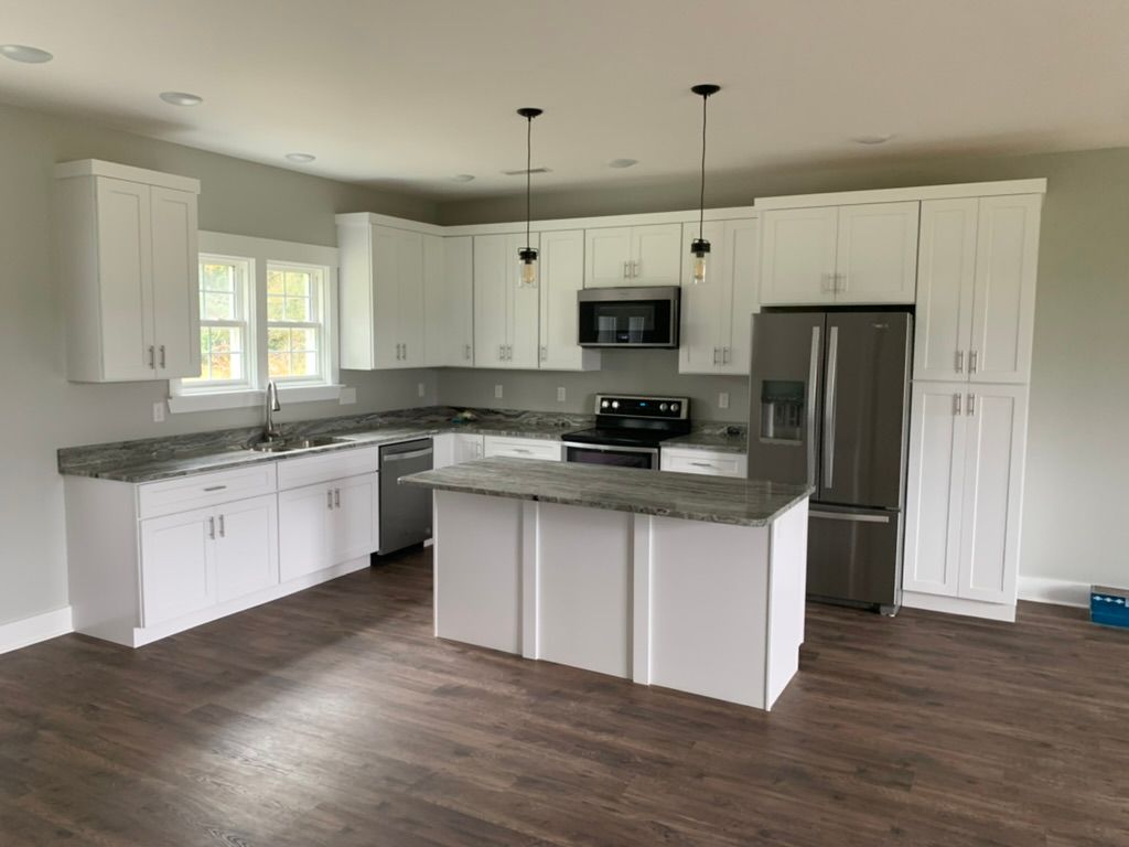 White kitchen with stainless steel appliances, gray countertops, and dark wood floor.