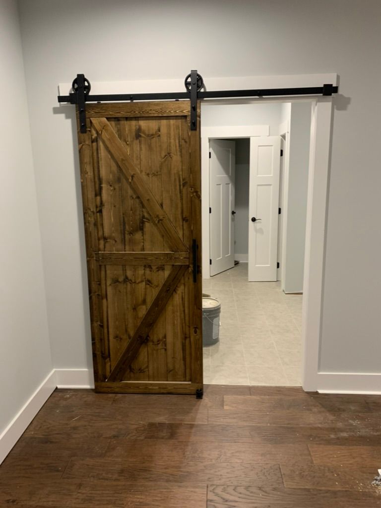 Barn door, stained wood, black hardware, in a room with wood floor, and doorways.