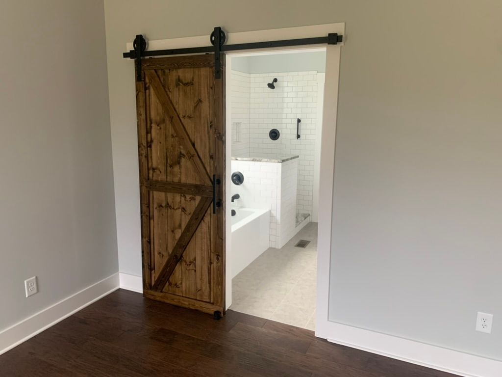 Barn door opens to a bathroom with a white tub, shower, and gray walls.