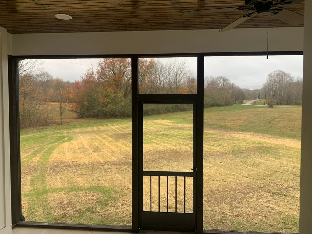 Screened porch with door open to a grassy field under a cloudy sky.