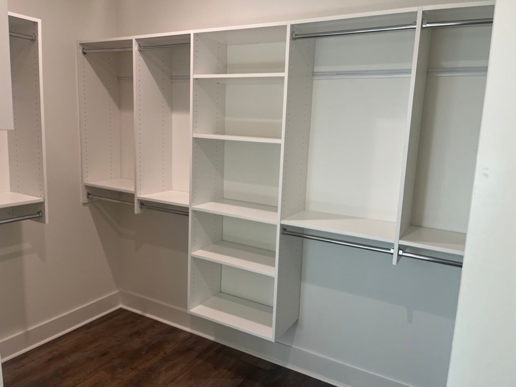 White closet shelving with hanging rods and shelves, on dark wooden floor.