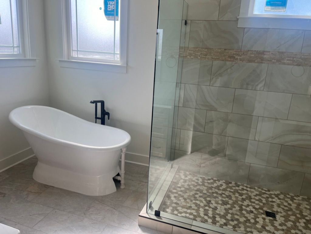 Bathroom with a white freestanding tub, shower with stone tile, and two windows.