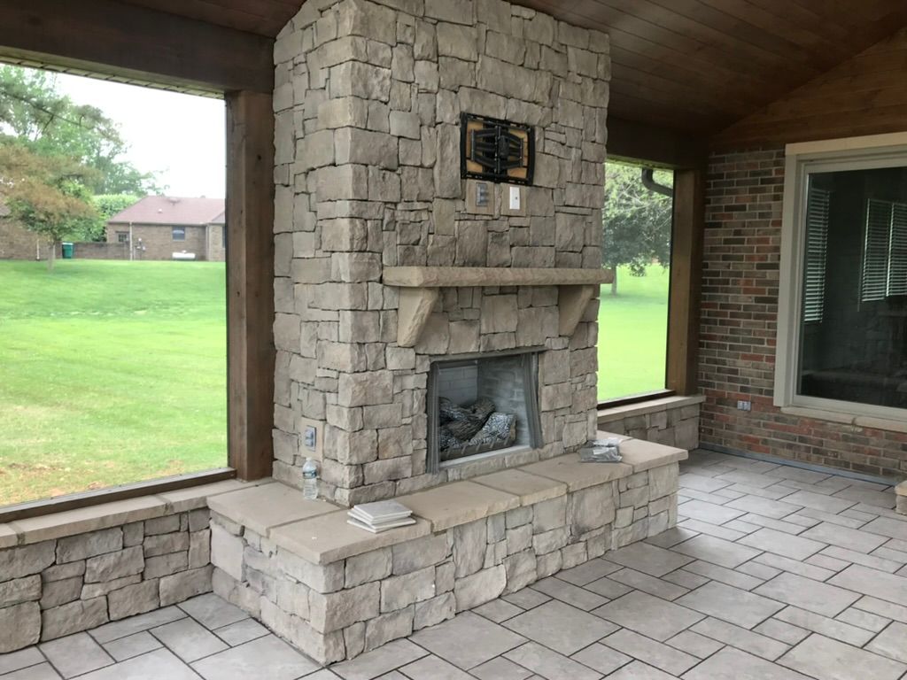 Stone fireplace in a sunroom with large windows overlooking a green lawn.