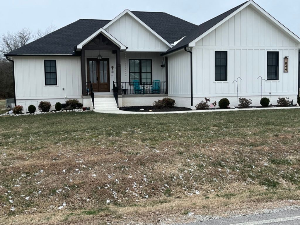 White farmhouse with black trim and a dark roof on a grassy lot.