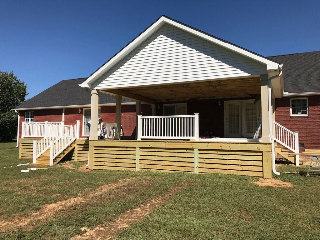 Wooden deck with white railing and covered porch attached to a brick house.