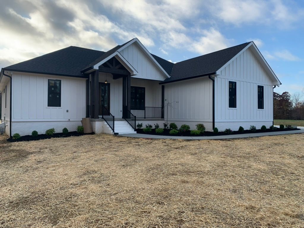 White farmhouse with black trim and roof; front porch, sparse landscaping.