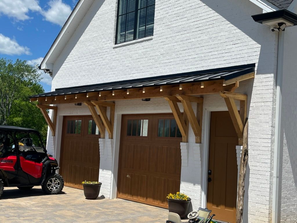 White brick garage with brown doors, wooden awning, and red vehicle.