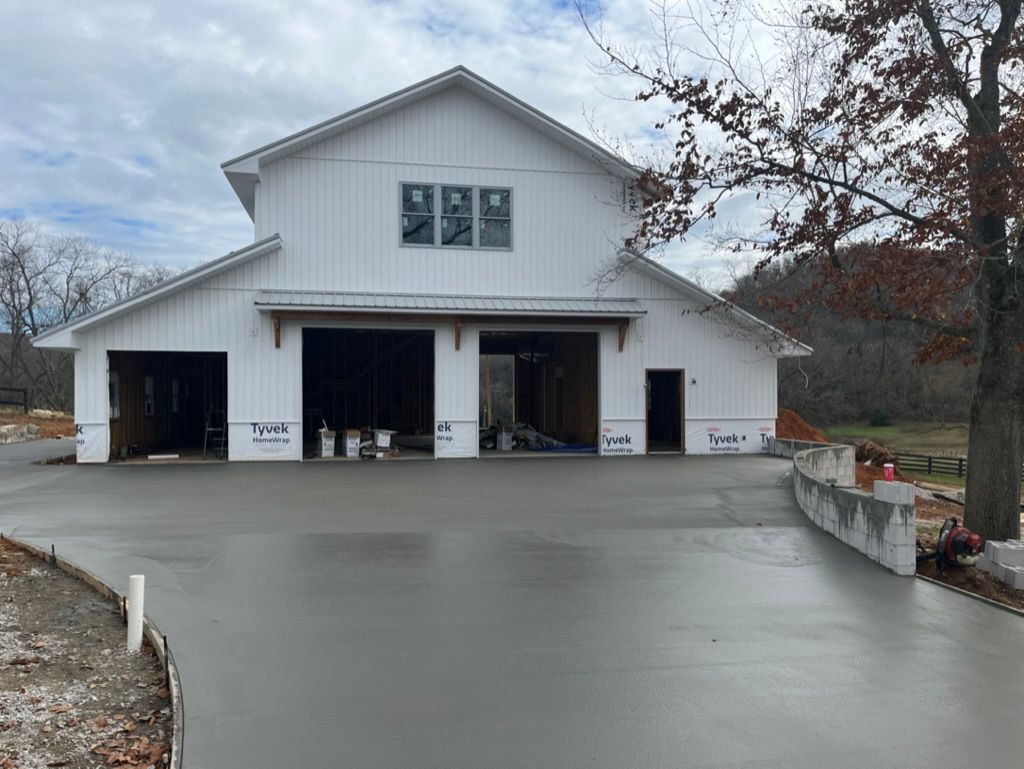 White barn with concrete driveway under construction on a cloudy day.