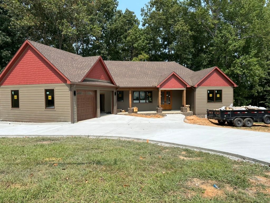 Beige house with red accents and a concrete driveway, parked trailer.