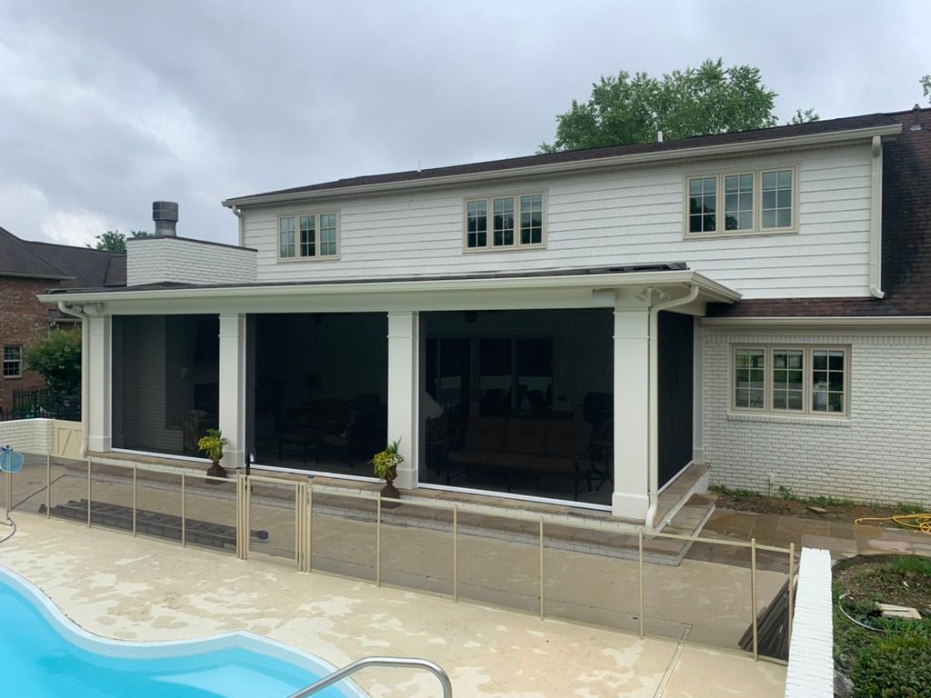 Back of a two-story white house with a screened porch, pool, and a safety fence.