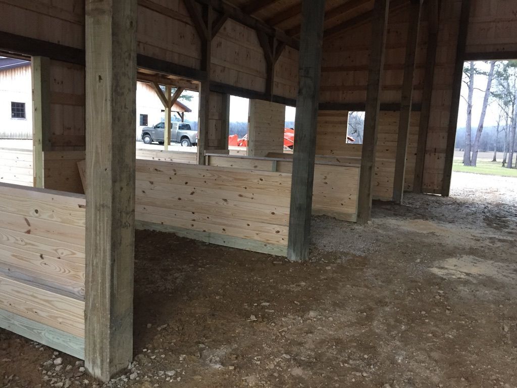 Interior view of a partially built barn with wooden stalls and dirt floor.