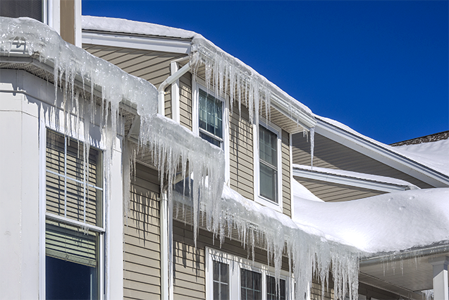 Icicles hang from a building's roof under a bright blue sky.