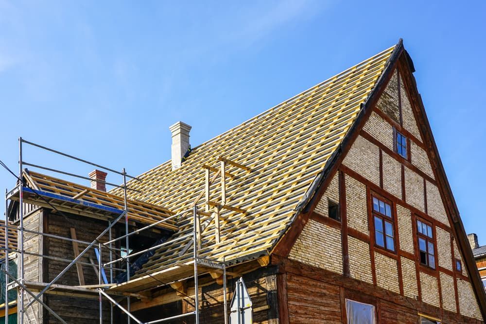 Half-timbered building with new roof tiles under construction; scaffolding on the side, blue sky.