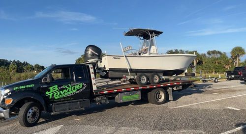 Truck towing a white boat on a trailer in a sunny parking lot with palm trees.