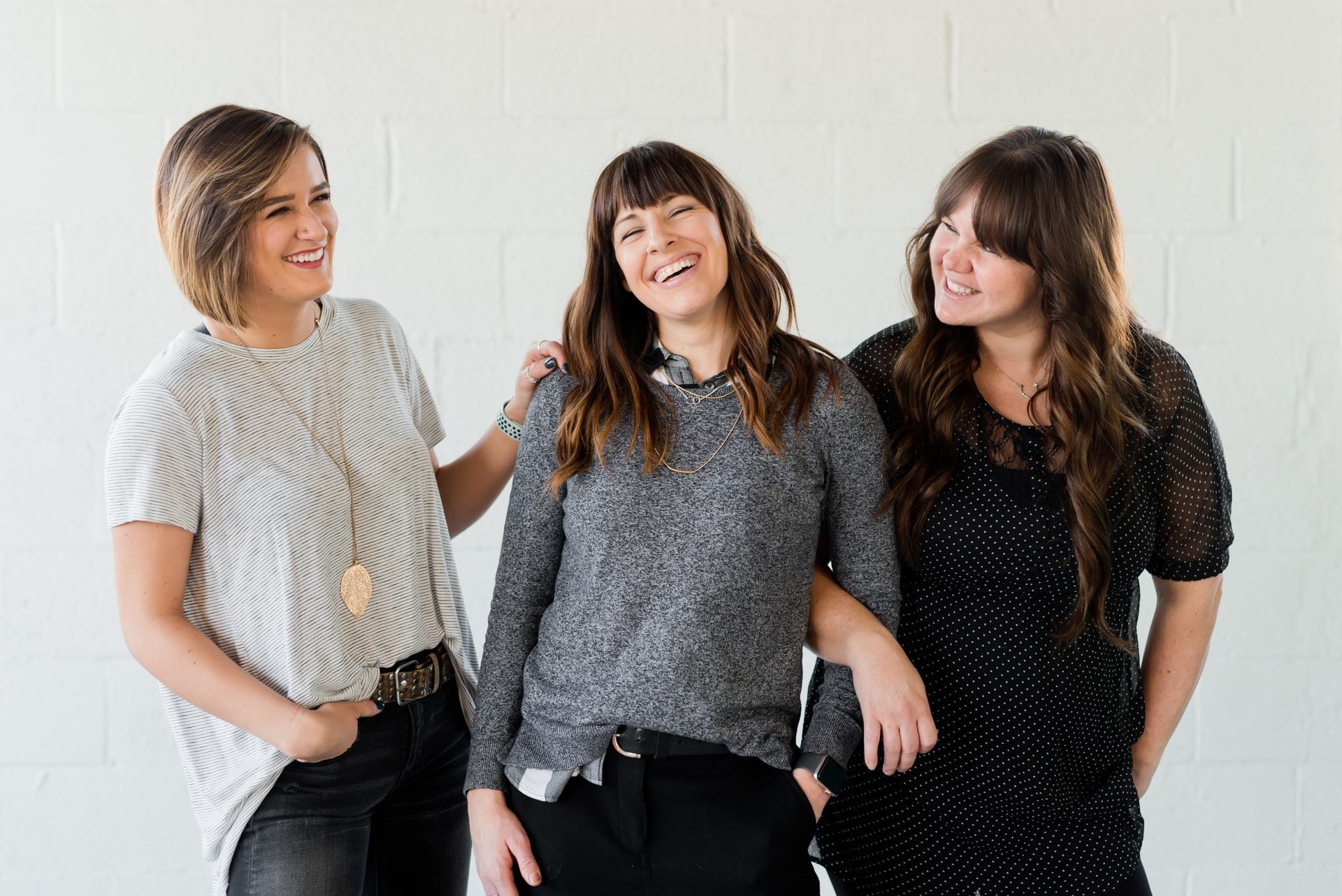 Three smiling women in casual attire, posing together against a white background.