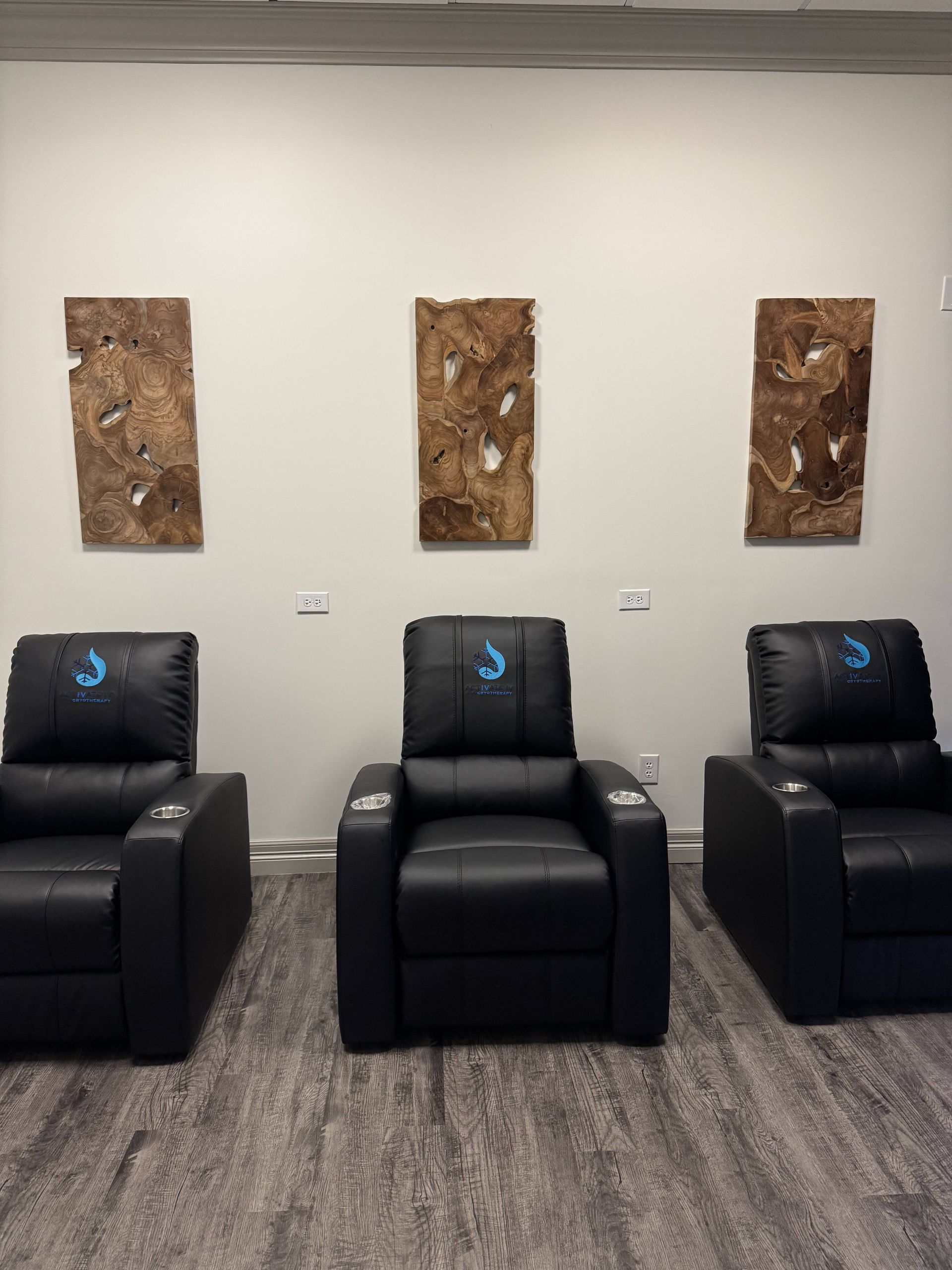 Three black recliners below three abstract brown wall art pieces in a room with gray carpet.