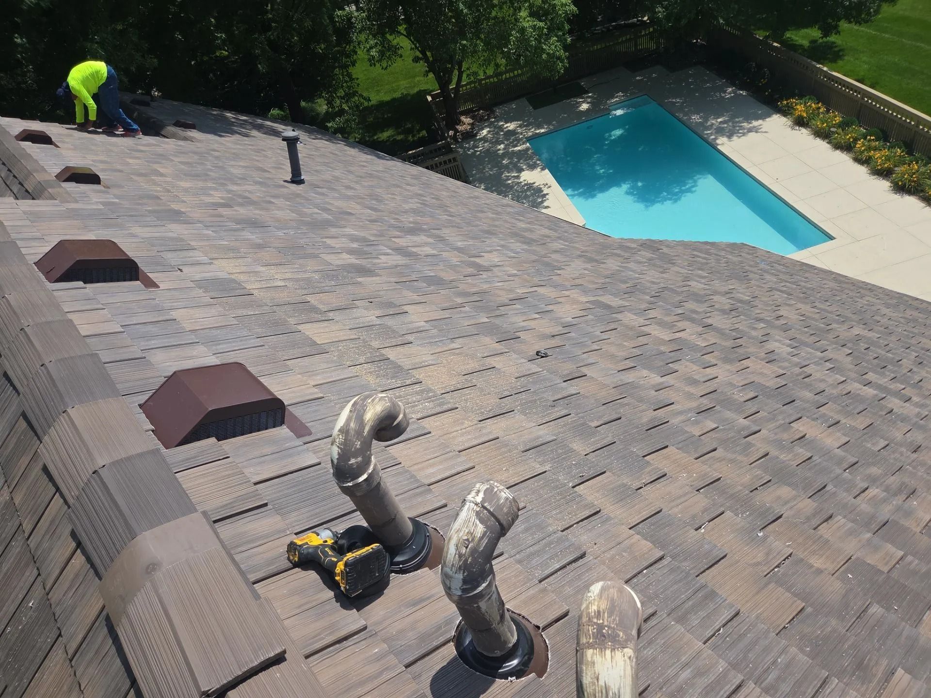 Roof with vents and a swimming pool in the background, a worker in a bright yellow vest is on the roof.
