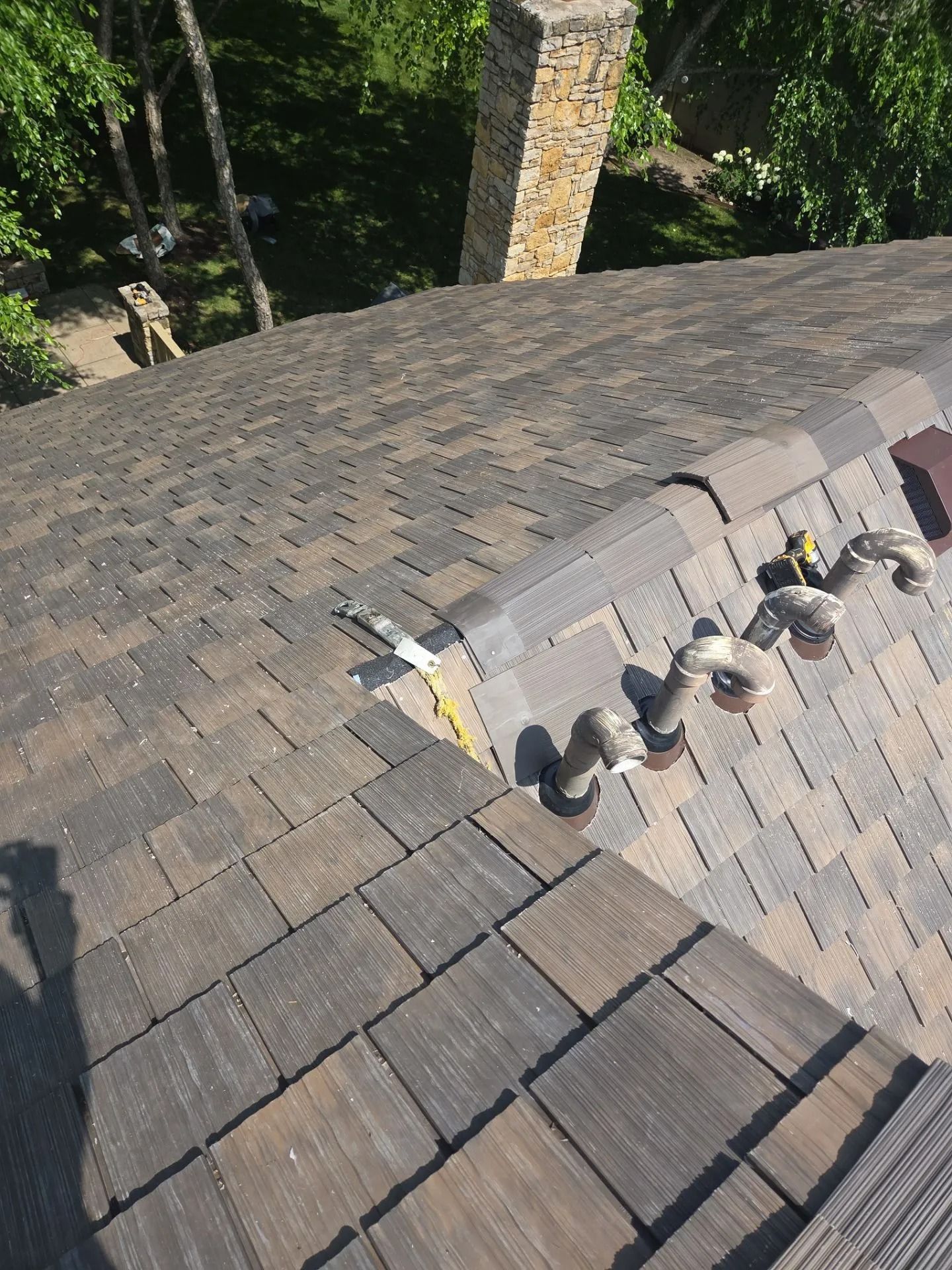 View of a rooftop with dark shingles, a brick chimney, and vent pipes.