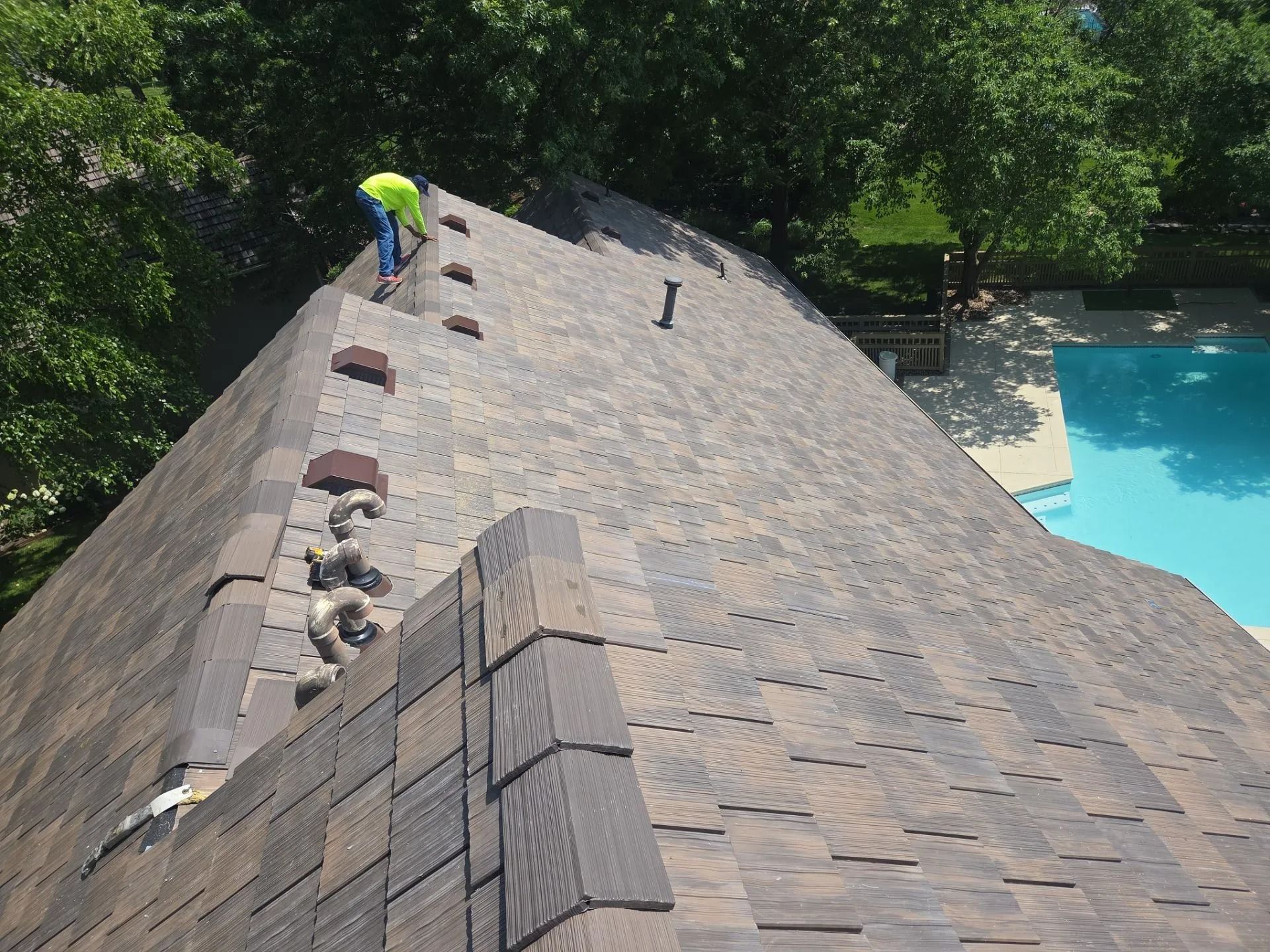 Roofer in yellow vest repairs roof with missing shingles next to a pool.