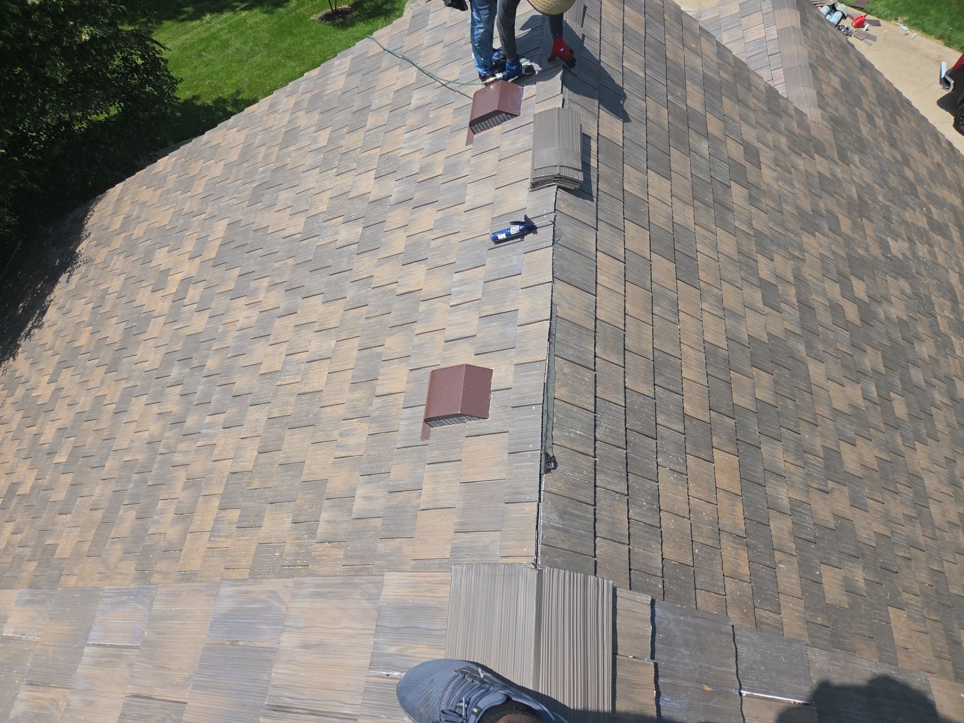 Overhead view of a roof with brown and tan shingles; two people are on the roof.