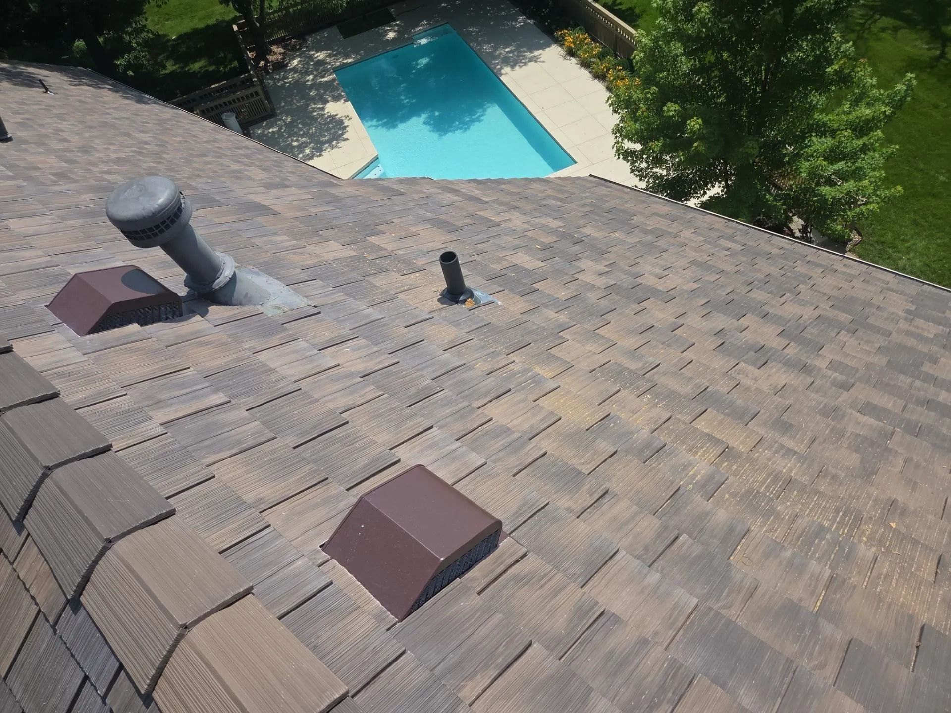 View of a roof with brown shingles, vents, and a backyard pool.