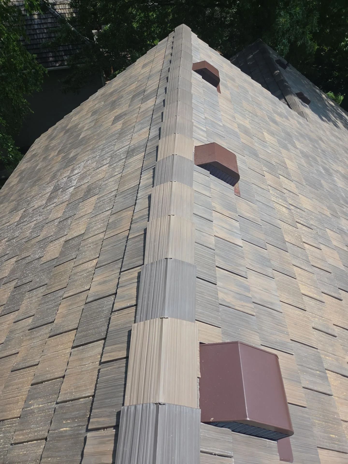 Close-up of a multi-colored shingle roof with three brown square vents, seen from above.