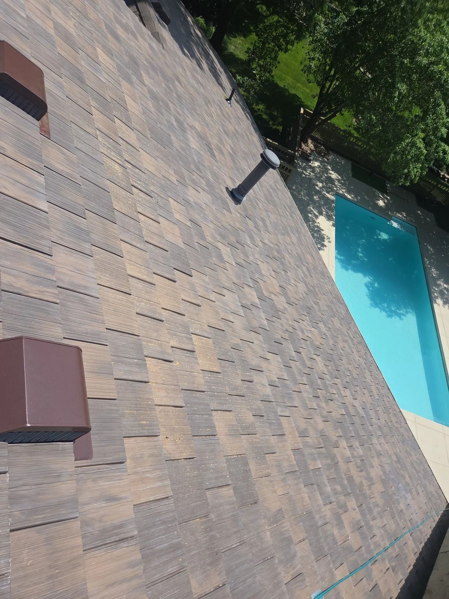 Brown asphalt shingle roof with vents, overlooking a pool with blue water.