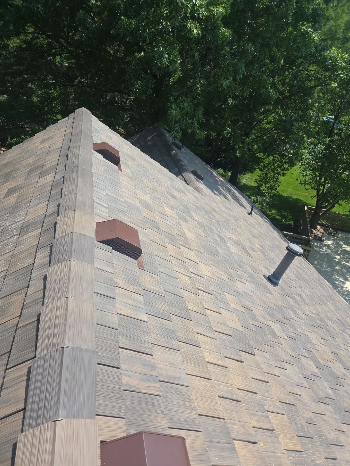Overhead view of a roof with brown and grey shingles, with two brick vents and a pipe.