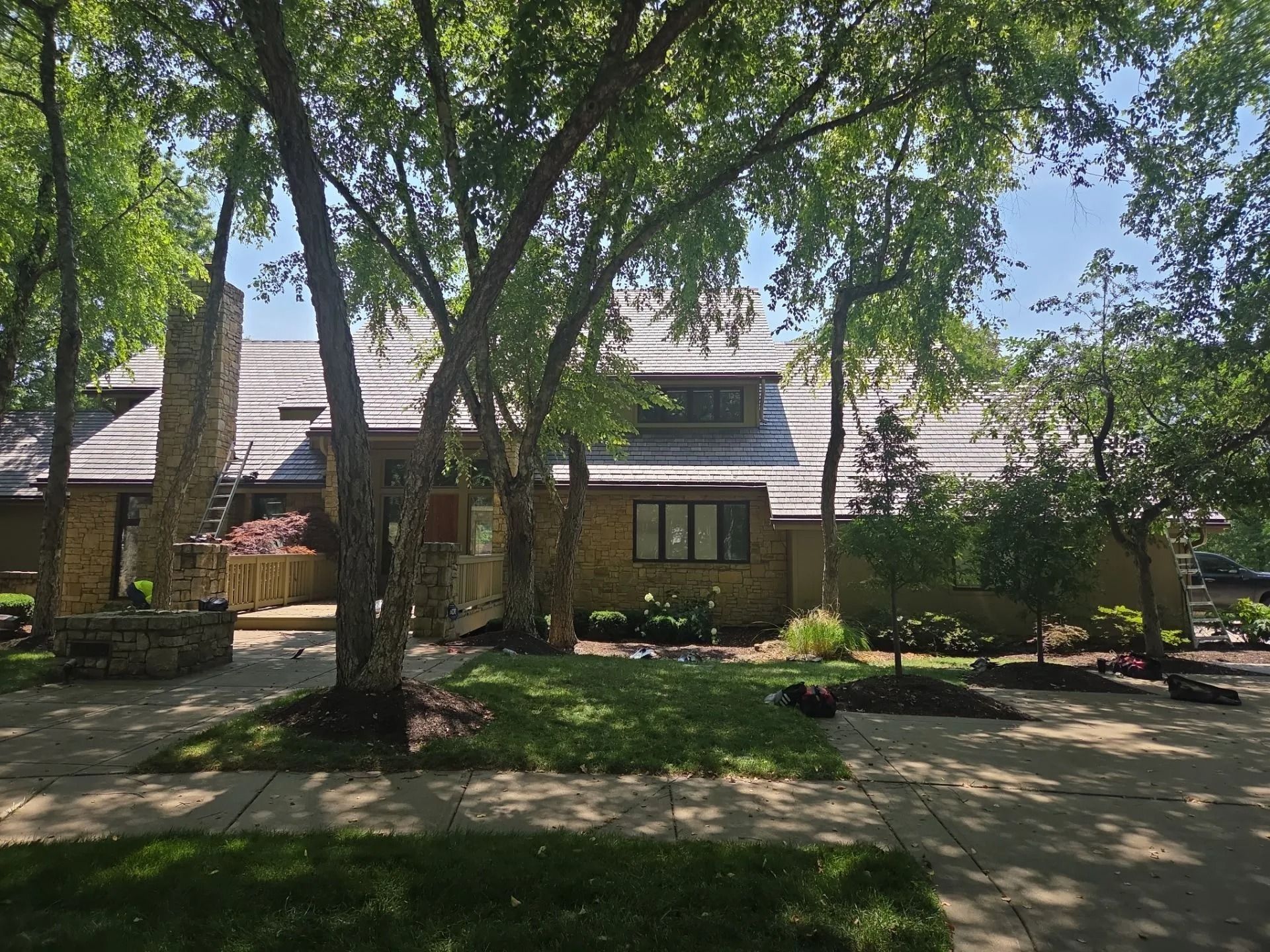 A single-story brick house with a stone chimney and a walkway lined with trees and bushes.