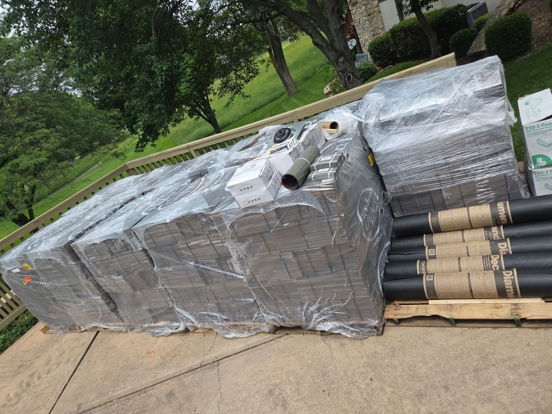 Pallet of wrapped construction materials on a driveway, including bricks and pipes.