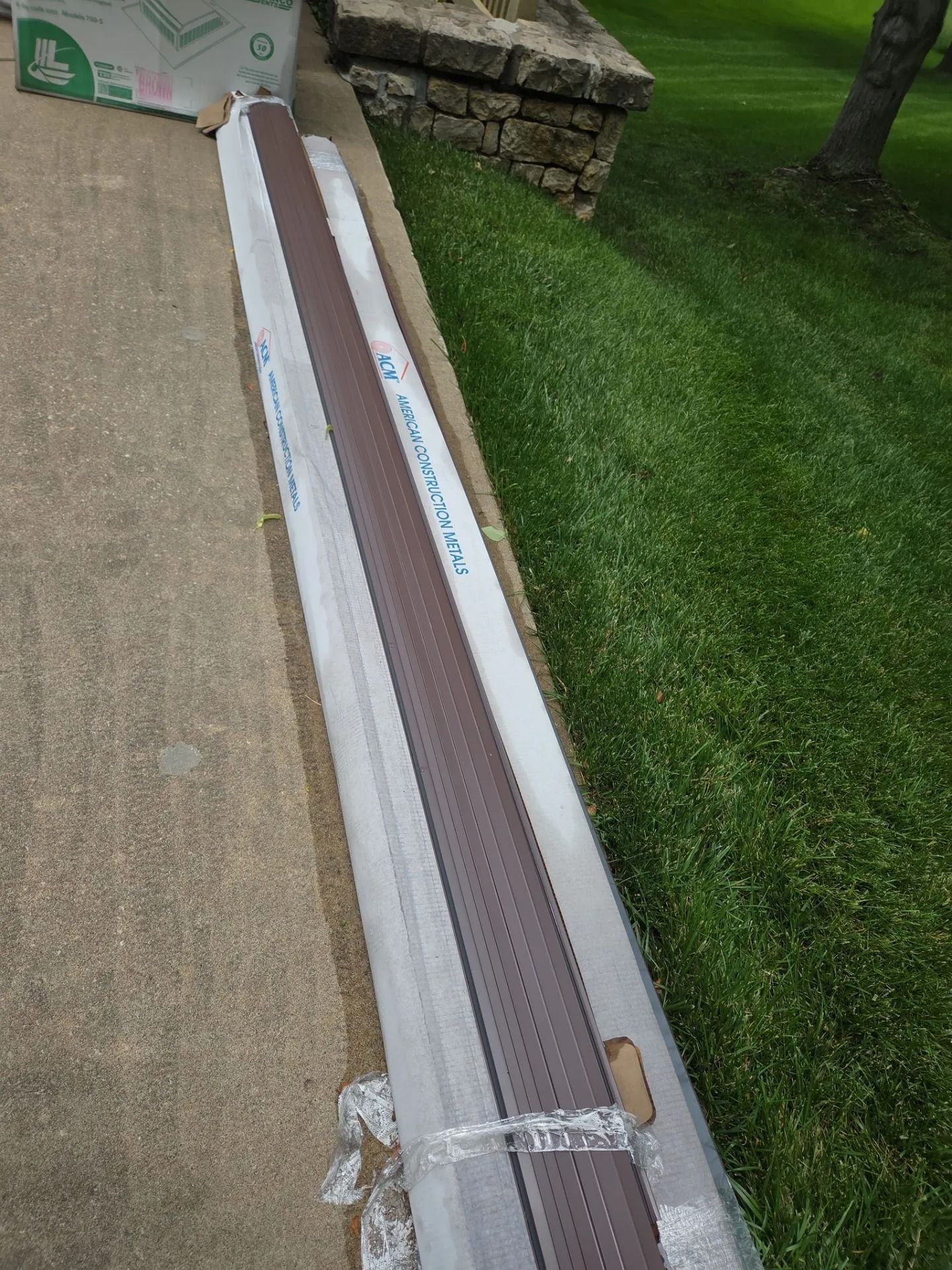 Brown gutter guard on concrete next to grass and a stone wall.