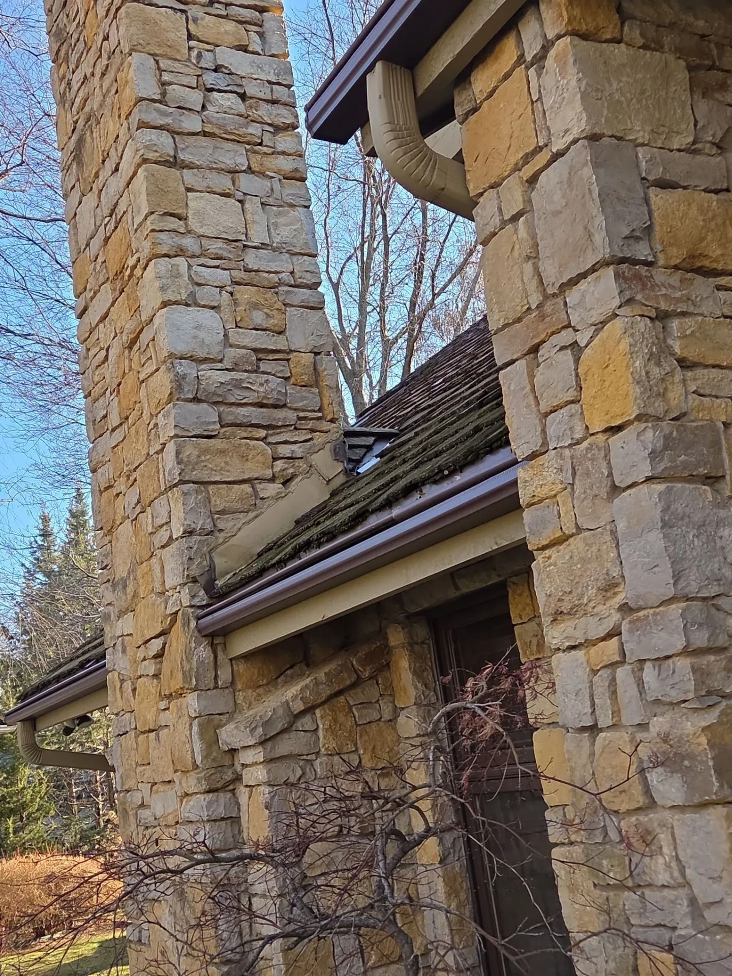 Stone chimney and building with brown gutters and roof against a blue sky.