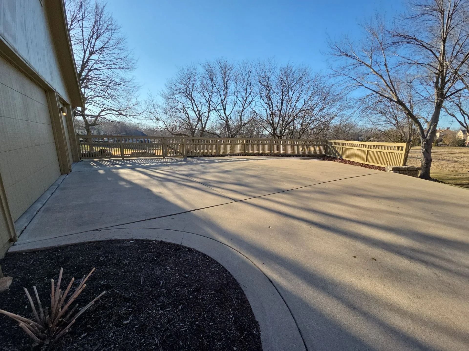Concrete patio with wooden fence and bare trees under a clear, sunny sky.