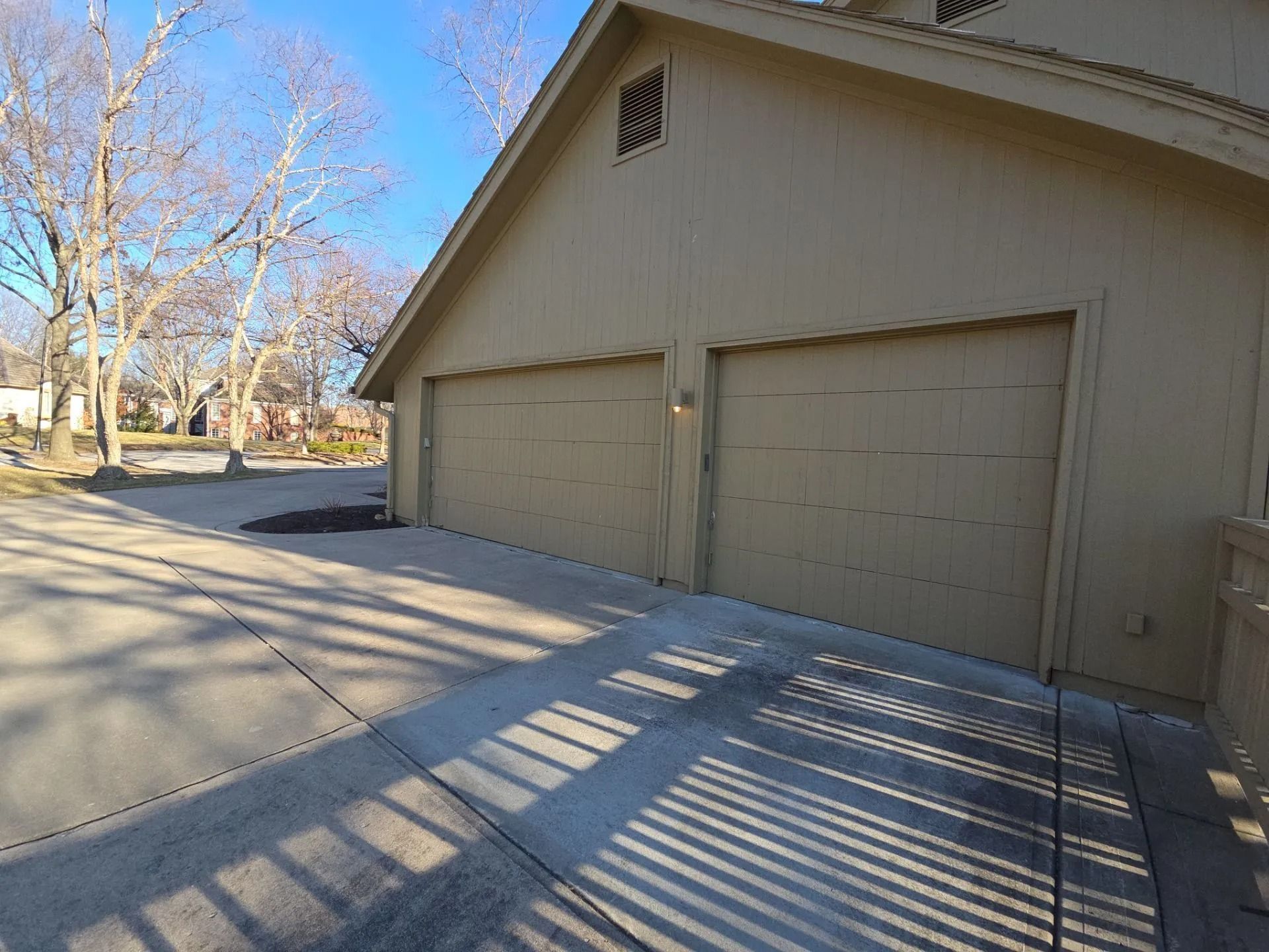 Tan garage with two doors on a sunny day. Long shadows cast across the concrete driveway.