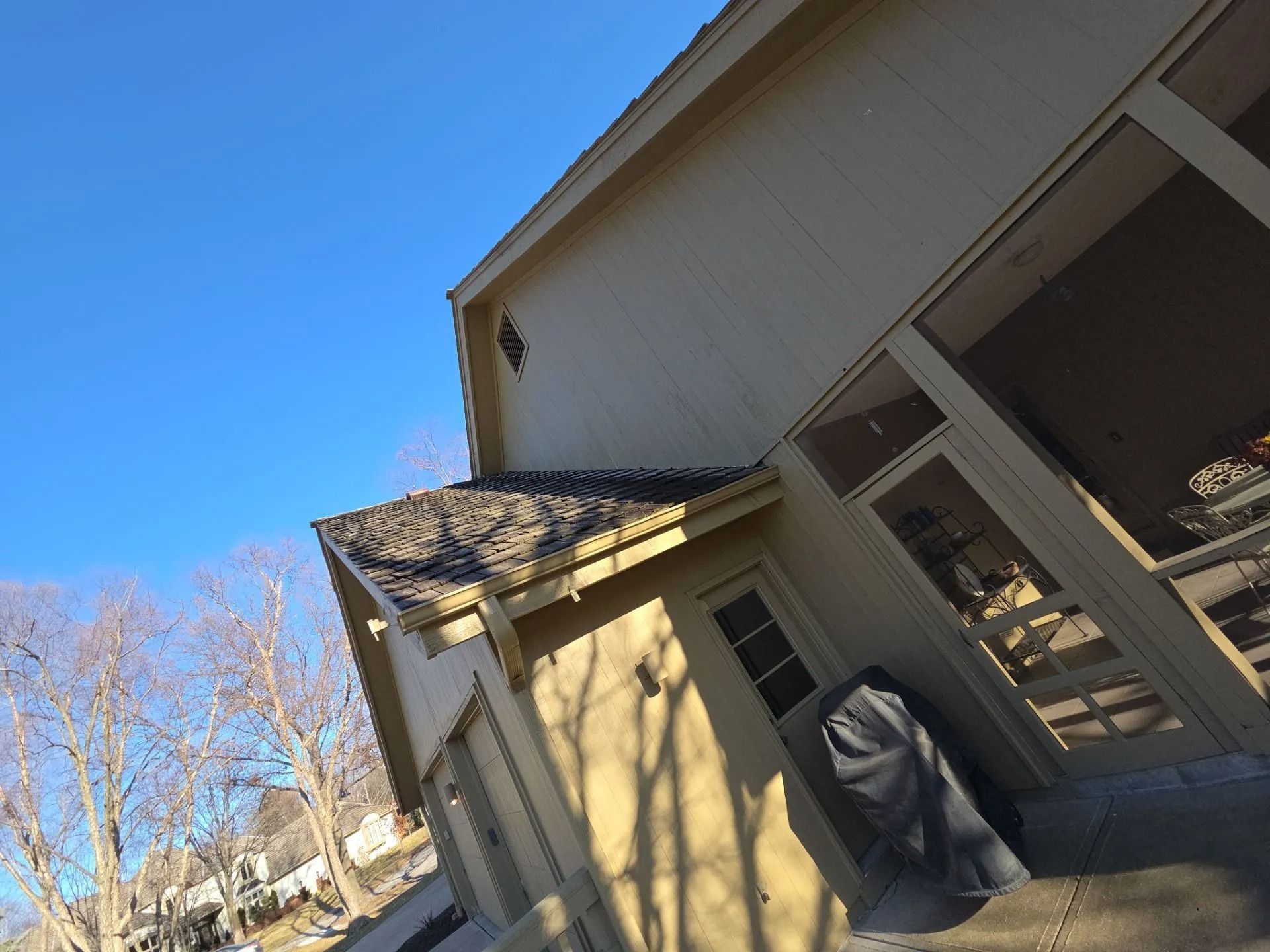 Beige house with a dark roof and large windows against a clear blue sky.