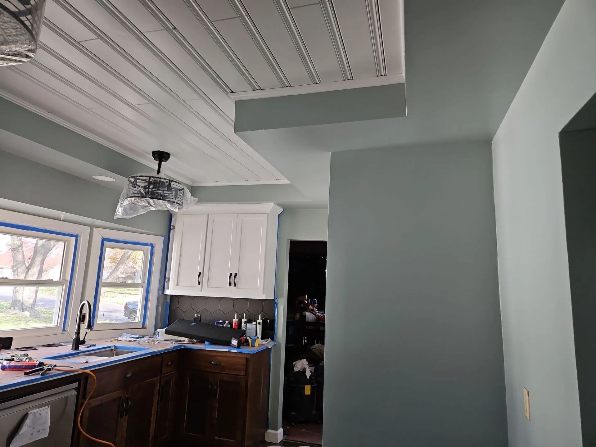 Kitchen with white cabinets, dark wood counter, blue-green walls, and a white, slatted ceiling.