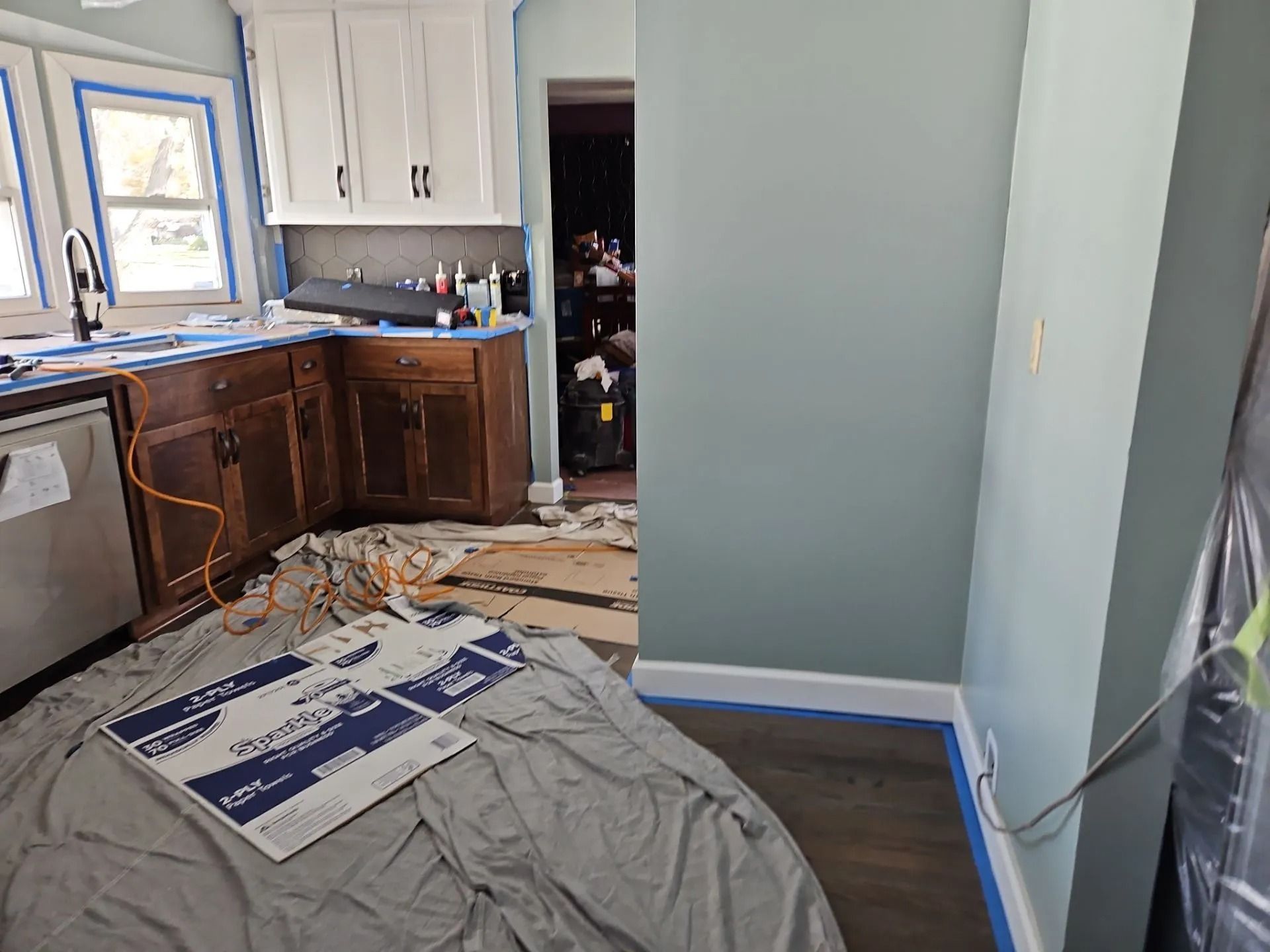 Kitchen renovation in progress: new white cabinets, dark wood lowers, blue walls, tools and materials scattered.